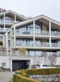Modern 3-story house, white exterior, large glass windows, multiple balconies, garage, driveway, landscaped garden