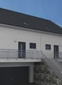 2-story house with a gray exterior, black roof tiles, large windows, balcony, and a garage on the ground floor.