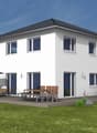 2 story house, white exterior, large windows, patio with outdoor furniture, garden, trees