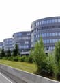 Multi-story office building with curved glass facade, surrounded by trees and a highway with cars passing by