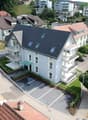 2-story residential building with modern architecture, featuring brown roofs, multiple balconies, and several visible parking spaces.