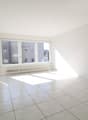 Empty room with white walls, white tiled floor, large window, white radiator