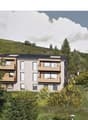 3-storey apartment building on hill, surrounded by greenery, large windows