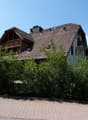 2 story house, brown roof, wooden balcony, brick wall, surrounded by bushes