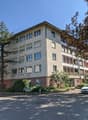 4 story building, multiple windows, red brick base, multiple balconies, trees, plants, car parked