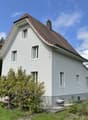 2 story house, white exterior, brown roof, large windows, front yard with greenery