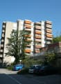 Large apartment building with balconies, orange awnings, surrounded by cars parked in designated parking spots.