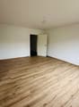 Empty room with wooden floor, white walls, two doors, one leading to another room, and a glass door leading to a balcony.