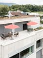 Modern white building with green roof terrace, solar panels, outdoor furniture, and an umbrella