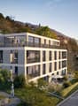 A modern, multi-story apartment building with balconies, surrounded by greenery and situated on a hillside overlooking a road and scenic mountain landscape.