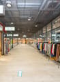 Shopping mall with glass walls, tiled floor, clothing stores, mannequins, clothing racks, and a blue arrow on the floor.