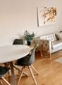 living room with sofa, round dining table, dining chairs, round coffee table, potted plant, wooden flooring, framed art on wall