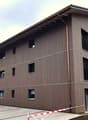 3 story building, brown exterior, multiple windows, parking area