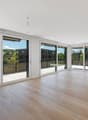 Spacious open-plan living area with large windows and sliding glass doors leading to a balcony, hardwood flooring, and a kitchen island.