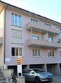 3-story apartment building with balconies, parking spaces in front, and a sign indicating the building's name or address