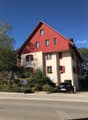 2 story house, red roof, white and red shutters, balcony, car parked in front