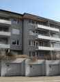 multi-story apartment building with balconies, grey exterior, multiple garages