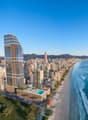 High-rise building with glass facade, swimming pool on the rooftop, surrounded by other buildings, beach, and ocean