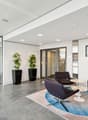 modern office lobby with glass walls, white walls, gray floor, two potted plants, three chairs, round table, carpet