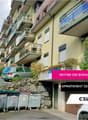 Multi-story apartment building with balconies, located in a residential area with trees and vegetation. The building has a sign indicating an apartment for rent on the 3rd floor.