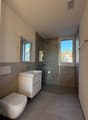 modern bathroom with white toilet, sink, shower, mirror, and tiled floor