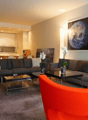 large living area with modern furnishings, 2 grey sofas, glass coffee tables, orange accent chair, large paintings on wall