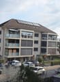 4 story building, solar panels on the roof, balconies, parking lot