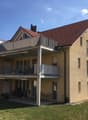 3-story apartment building with beige exterior, red tile roof, and balconies on each floor.