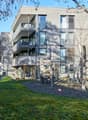 Modern apartment building, concrete exterior, glass windows, balconies on multiple floors, greenery around