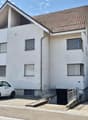 Apartment building with garage, white exterior, red tile roof, solar panels, small car parked in front