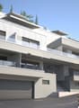 3-story modern apartment building with a gray and white exterior, balconies, and a garage on the ground floor. The building is surrounded by trees and has a sloped driveway leading up to the entrance.