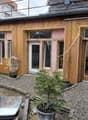 Wooden exterior, pink painted wall, 3 windows, balcony on top floor, gravel driveway, partially completed