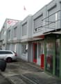 Commercial building with multiple windows, red door, green door, balcony, cars parked in front