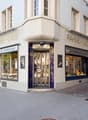 Facade of a building with glass windows and doors, name Rahme-Lade, people walking on the sidewalk
