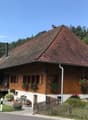 Rustic 2-story house, wooden exterior, terracotta roof, several windows, surrounded by greenery and flowers, wooden fence and pathway