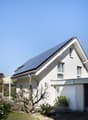 white house, solar panels on the roof, small garden, brick driveway