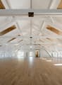 large open space, wooden floor, white walls, white beams, windows, wooden ceiling