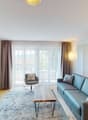 a large living room with windows, couch, sofa, desk, TV, floor lamp, wall lamp