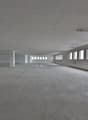 Large open space with concrete floor, white walls, and multiple windows along the sides. The space appears to be an unfinished commercial or industrial building, possibly a warehouse or factory.