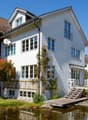 2 story house, white exterior, brown roof, large windows, wooden deck, small pond, garden