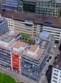 Urban area with multiple buildings, multistory parking, solar panels, various roof types, trees, street traffic