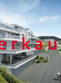An apartment building made of white material, with many balconies, greenery, and parking area