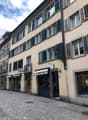 4 story beige building, green shutters, street lamp, entrance to shops
