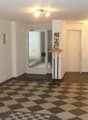 White walls, checkered flooring, wooden bench, glass door, white doors, hanging coat rack, picture frames on wall