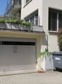 white building with balcony, glass door, signboard, trash bin