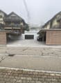 Apartment building with carport, driveway, two garages with closed doors, and two covered parking spaces.