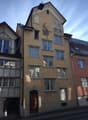 A four story residential building made of bricks, a balcony with an awning, windows with shutters
