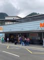 Front entrance of the Migros store with glass walls and doors, many people are entering