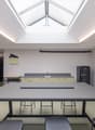 Empty kitchen area with a long table, stools, countertop, sink, and a refrigerator.