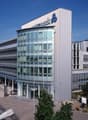modern office building, glass facade, multiple floors, large parking lot, trees, cars parked